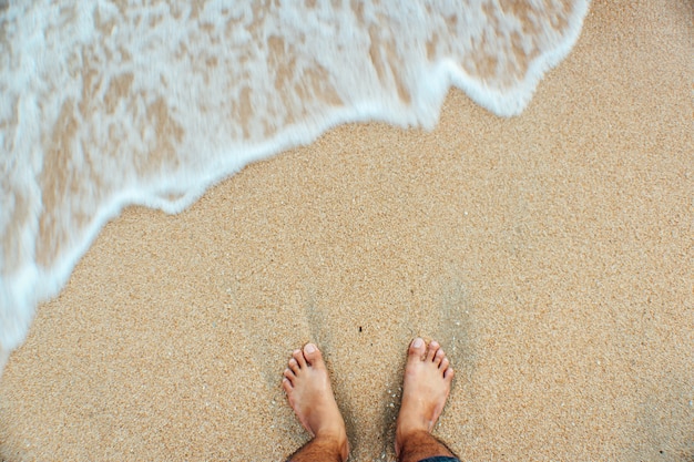 Die Beine des Mannes auf dem Sandstrand und den Meereswellen