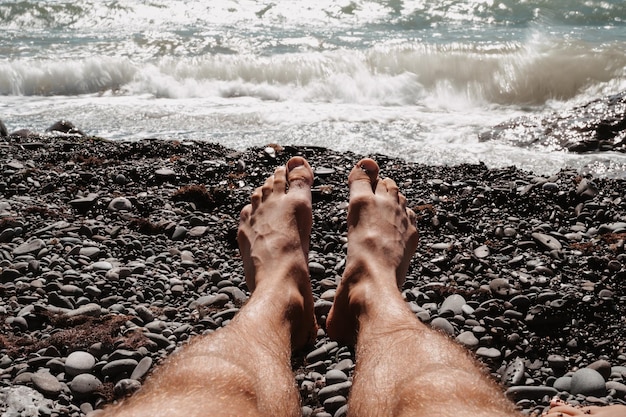 Die Beine des Mannes Nahaufnahme an einem sonnigen Strand am Wasser Ruhen Sie sich am Meer aus