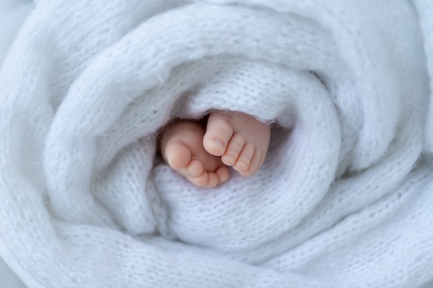 Die Beine des Neugeborenen eingewickelt in weißes weiches Tuch nah oben.