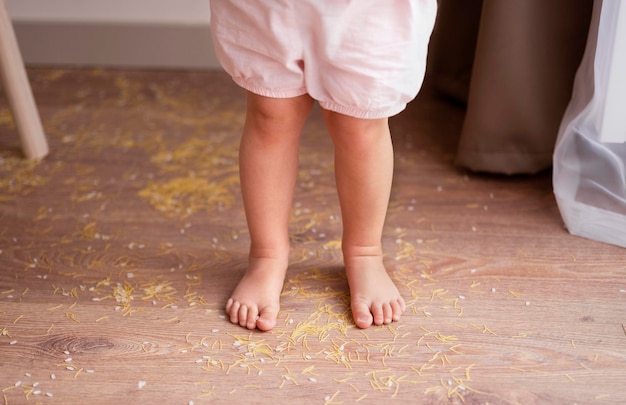 Die Beine eines Kleinkindmädchens stehen auf einem unordentlichen Boden, nachdem sie mit Getreidenüssen, Nudeln und Reis gespielt haben. Sensorische frühe Entwicklungserziehung für Kleinkinder