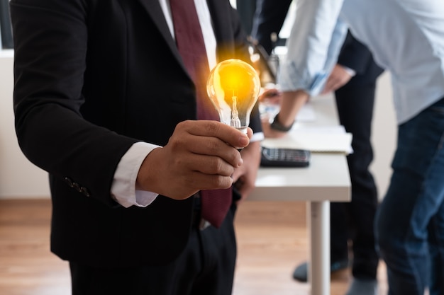 Die beleuchtete Glühbirne in der Hand eines Geschäftsmanns vergleicht seine neue Idee