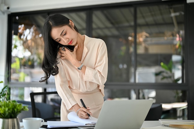 Die beschäftigte und konzentrierte tausendjährige asiatische Geschäftsfrau telefoniert in ihrem Büro