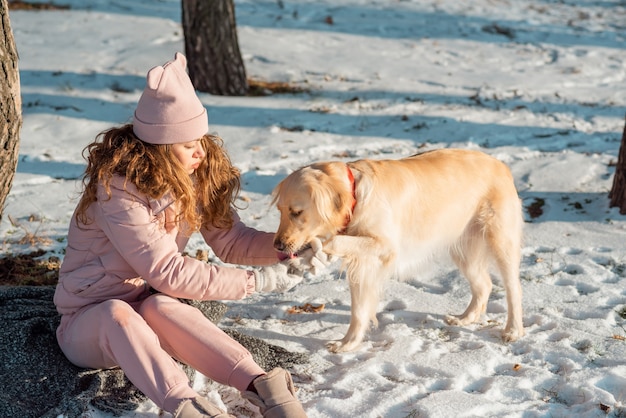 Die Besitzerin hilft ihrem schönen Hund Golden Retriever, die Pfoten zu räumen. Die Pfoten des Hundes frieren im Winter und der Schnee ist verstopft.