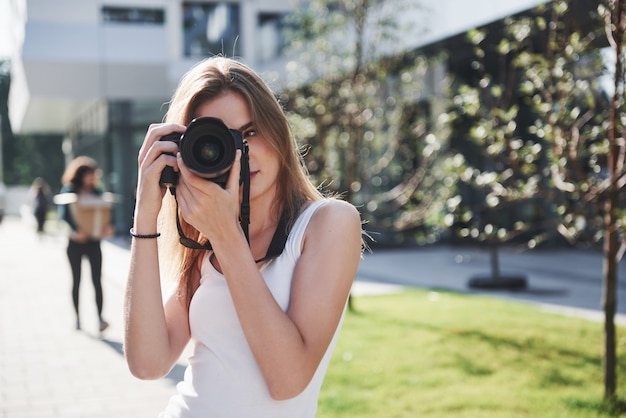 Die Bloggerin der Fotografin hält eine professionelle Kamera im Freien in der Stadt in der Hand