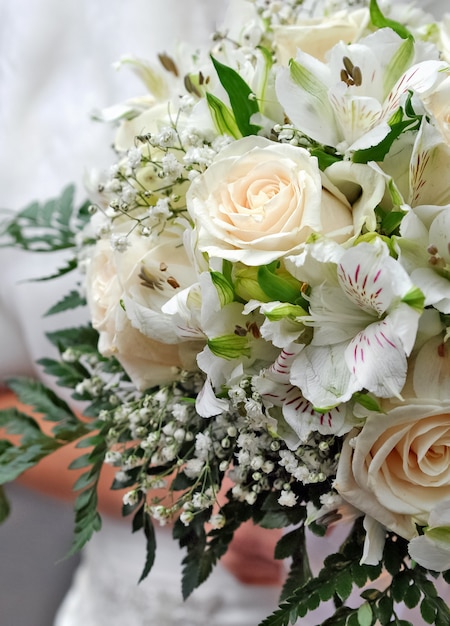 Die Braut hält einen Hochzeitsstrauß aus cremefarbenen Rosen und Lilien