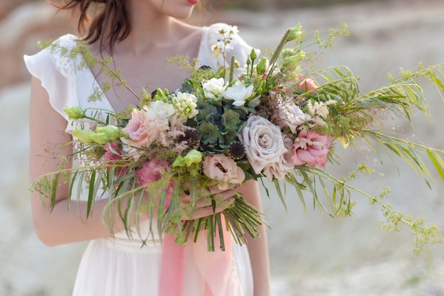 Die braut hält einen hochzeitsstrauß mit ungewöhnlich schönen blumen in der hand