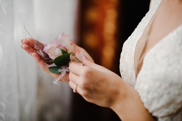 Die Braut hält in der Hand Nahaufnahme der Knopflochblumen des Bräutigams und Grün und Grün.