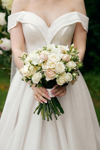 Die Braut im Brautkleid mit offenen Schultern hält einen Rosenstrauß