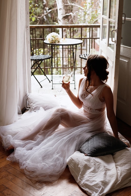 Die Braut im Penioire sitzt mit einem Glas Champagner auf dem Balkon