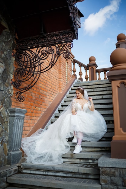 Die Braut im weißen Brautkleid und weißen Turnschuhen sitzt auf den Stufen eines großen Gebäudes