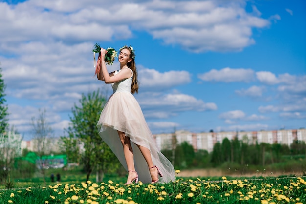 Die Braut im weißen Hochzeitskleid hält einen Blumenstrauß im grünen Park