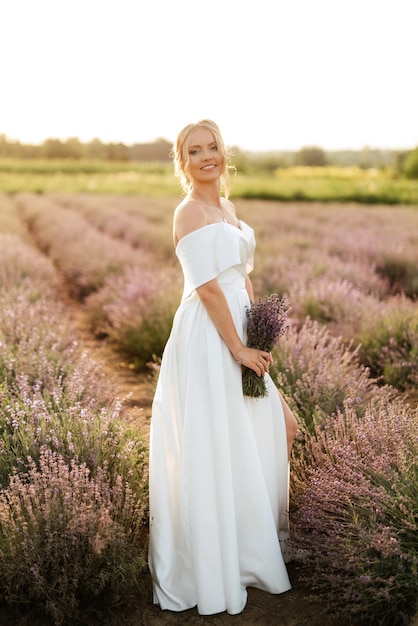 Die Braut im weißen Kleid geht über das Lavendelfeld