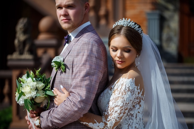 Die Braut in einem weißen Hochzeitskleid und der Bräutigam in einem Anzug auf dem Hintergrund eines Backsteingebäudes mit großen Stufen