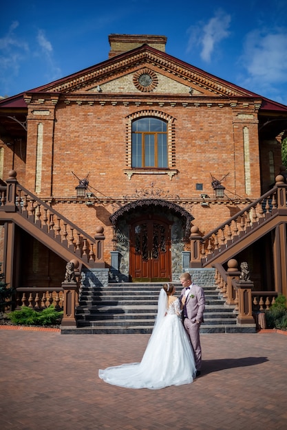 Foto die braut in einem weißen hochzeitskleid und der bräutigam in einem anzug auf dem hintergrund eines backsteingebäudes mit großen stufen
