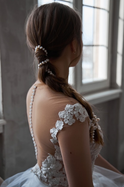 Die Braut ist eine Frau in einem leichten Sommerhochzeitskleid, die am Fenster steht.