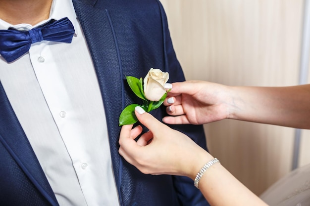 Die Braut legt dem Bräutigam am Hochzeitstag einen Boutonniere aus weißen Rosen an
