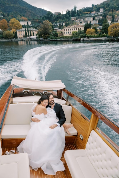 Die Braut sitzt auf dem Schoß des Bräutigams und umarmt ihn, während sie auf einer Yacht auf dem Lake Como in Italien segelt