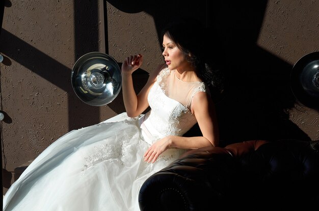 Foto die braut sitzt auf dem sofa und schaut aus dem fenster sonnenstrahl hochzeitskleid hochzeit