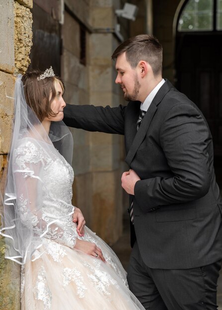 Die Braut steht zu Hause an der Mauer eines alten Schlosses und blickt sanft auf die Hochzeitsliebe des Bräutigams