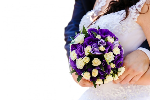 Die Braut und der Bräutigam, die einen Hochzeitsblumenstrauß von weißen und purpurroten Blumen halten