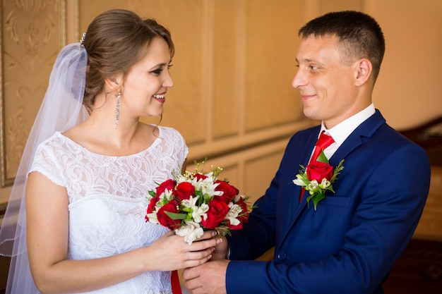 Die Braut und der Bräutigam, die im Hotelzimmer, einen Hochzeitsblumenstrauß halten küssen