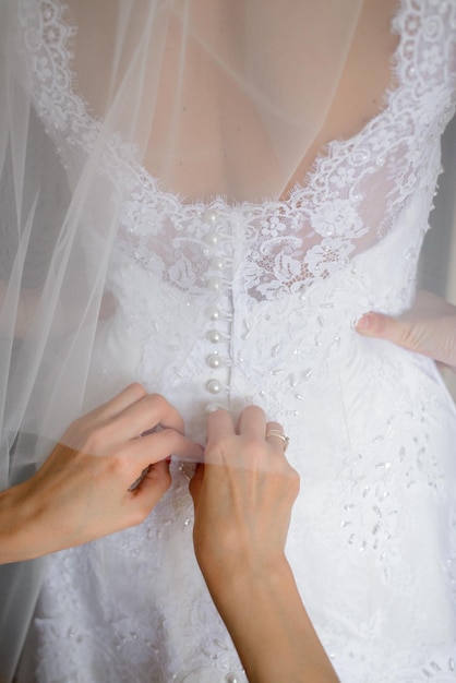 Die Brautjungfern helfen der Braut, ihr Hochzeitskleid anzuziehen Nahaufnahme der Hände