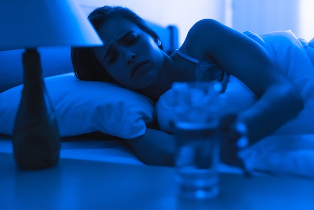 Die depressive Frau auf dem Bett hält eine Alkoholspritze in der Hand. abend nacht zeit