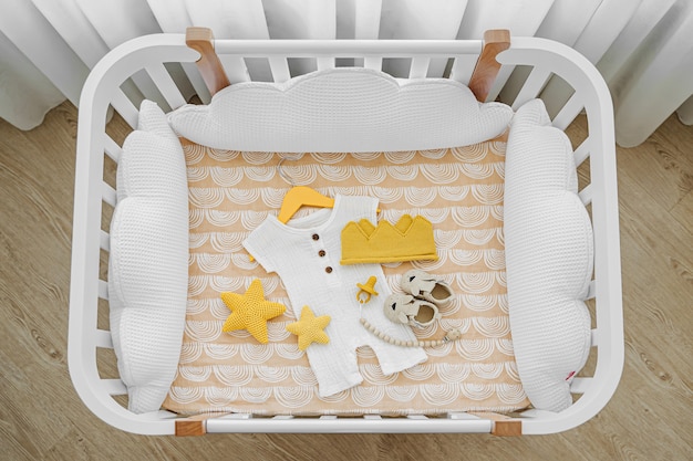 Die Draufsicht auf Babykleidung und Zubehör im Kinderbett, Wiege. Holzwiege für Neugeborene mit weißen Kissen im Babyzimmer.