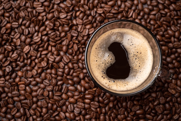 Die Draufsicht auf eine Kaffeetasse und eine Gruppe schwarzer Kaffeebohnen ist der Hintergrund