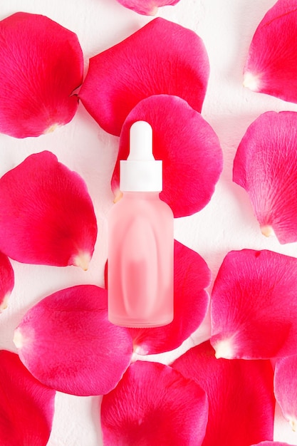 Die Draufsicht auf eine weiße, matte Flasche mit Pipette und weißem Verschluss mit einem natürlichen Kosmetikserum oder -öl liegt auf frischen Rosenblättern