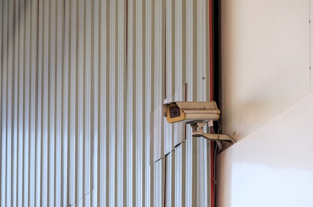 Die dreckige Sicherheits-Videokamera hängt hoch am Eingang der Lagerhalle im Industriepark, Frontansicht für den Hintergrund.