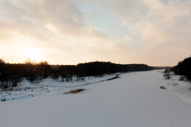 Die eis- und schneebedeckte Oberfläche des Flusses bei Sonnenuntergang, gefroren in der Wintersaison