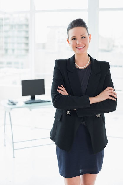 Die elegante Geschäftsfrau, die mit den Armen steht, kreuzte im Büro