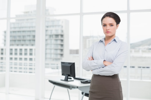 Die elegante Geschäftsfrau, die mit den Armen steht, kreuzte im Büro