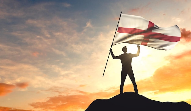 Die englische Flagge wird von einem Mann geschwenkt, der den Erfolg auf der Spitze eines Berges feiert 3D-Rendering