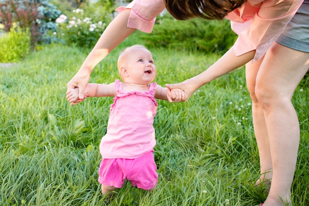 Die ersten Schritte eines kleinen Mädchenkindes Mama und kleine blonde Tochter haben Spaß im Freien