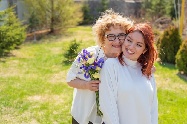 Die erwachsene Tochter schenkt ihrer Mutter Blumen draußen im Hof des Hauses und verbringt am Wochenende gemeinsam Zeit beim Feiern zu Hause. Muttertag. Herzliche Beziehungen zwischen den Generationen