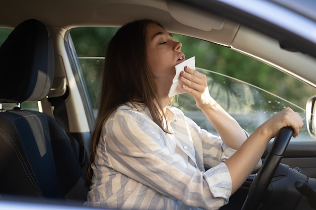 Die Fahrerin, die während der Hitzewelle im Auto unter heißem Wetter leidet, wischt Schweiß von der Stirn
