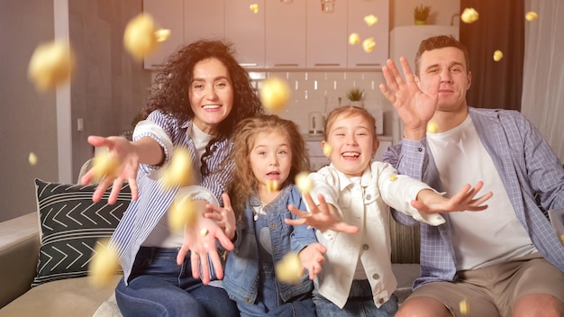 Die Familie, die das Wochenende genießt, sitzt auf dem Sofa und wirft Popcorn