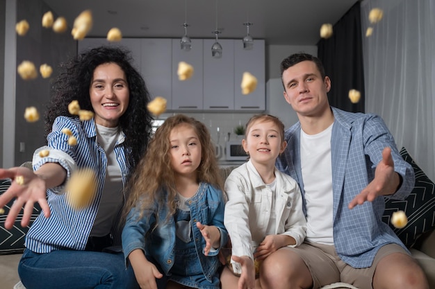 Die Familie, die das Wochenende genießt, sitzt auf dem Sofa und wirft Popcorn