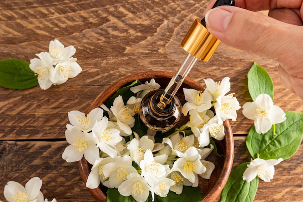 Die Finger der Hand einer Frau halten eine Pipette mit einer Bio-Kosmetik auf Basis von Jasminöl Holzhintergrund weiße Jasminblüten