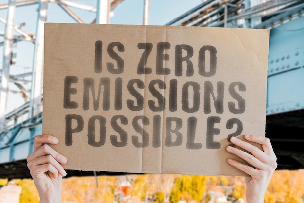 Die Frage "Ist Zero Emission möglich?" auf einem Banner in Männerhand mit verschwommenem Hintergrund. Krise. Ökologisch. Erwärmen. Gesellschaft. Umweltfreundlich. Energie sparen. Produktion