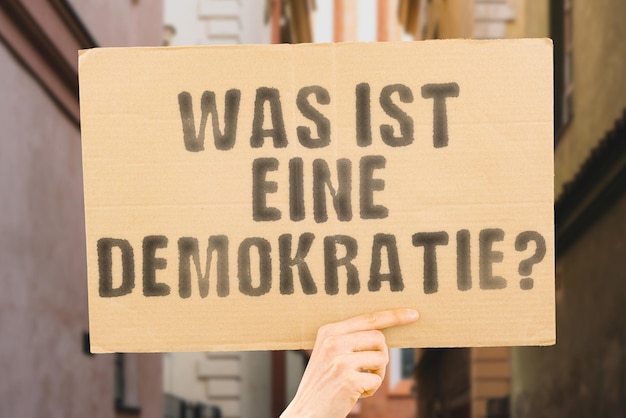 Die Frage, was eine Demokratie ist, steht auf einem Banner in den Händen der Männer mit verschwommenem Hintergrund Toleranzdebatte Kompromissverhandlungen Koalitionsbewusstsein Bildung Advocacy-Kampagne