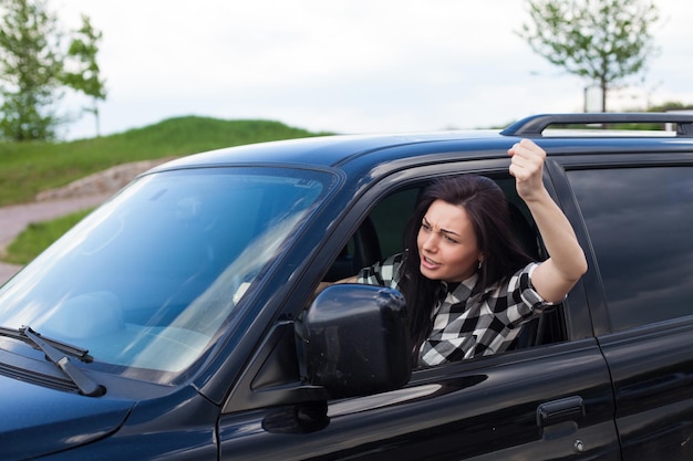 Die Frau beschimpft jemanden und hält ein Autorad und zeigt eine Faust eines schwarzen Autos