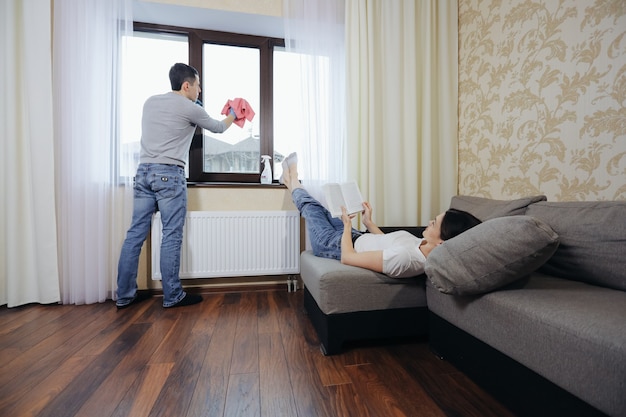 Die Frau beutet ihren Mann aus. Sie liest ein Buch und befiehlt, das Fenster zu putzen