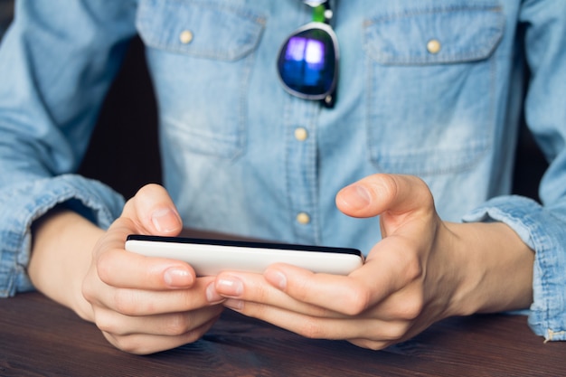 Die Frau, die einen Handy hält, wird sie in einem Denimhemd und in einer Sonnenbrille gekleidet