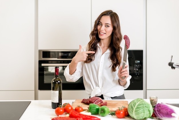 Die Frau, die frisches rotes Fleisch zeigt, das sie auf der Küche kocht