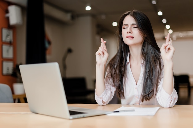 Die Frau, die mit den Fingern hofft und betet, kreuzte nahe Laptop