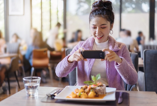 Die Frau, die Smartphone verwendet, machen Foto des Lebensmittels, bevor Sie im Restaurant essen