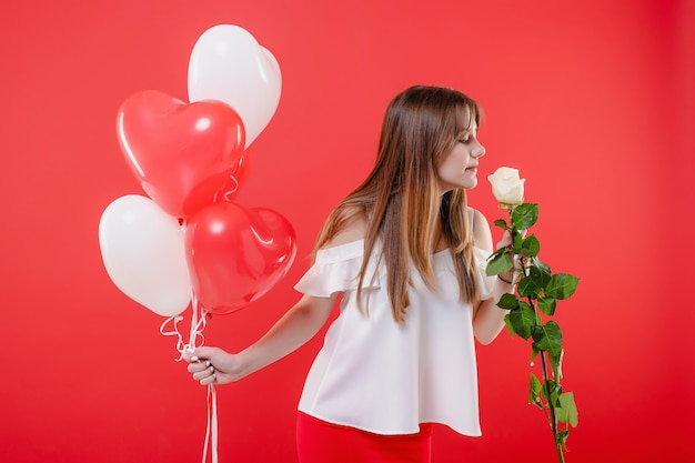 Die Frau, die Weißrose und Herz riecht, formte die Ballone, die über roter Wand lokalisiert wurden